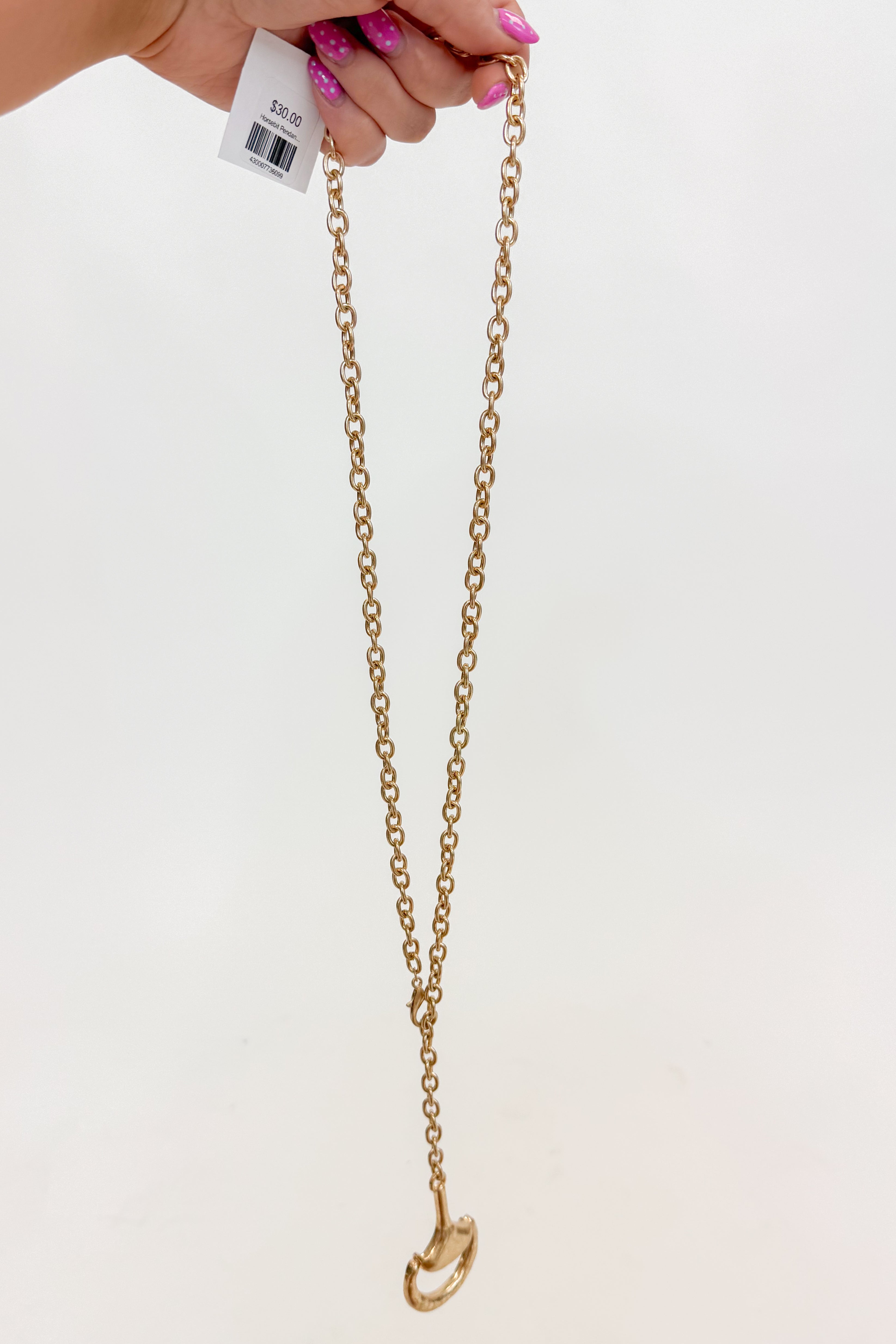 Gold chain necklace held by a hand with pink nail polish on a white background