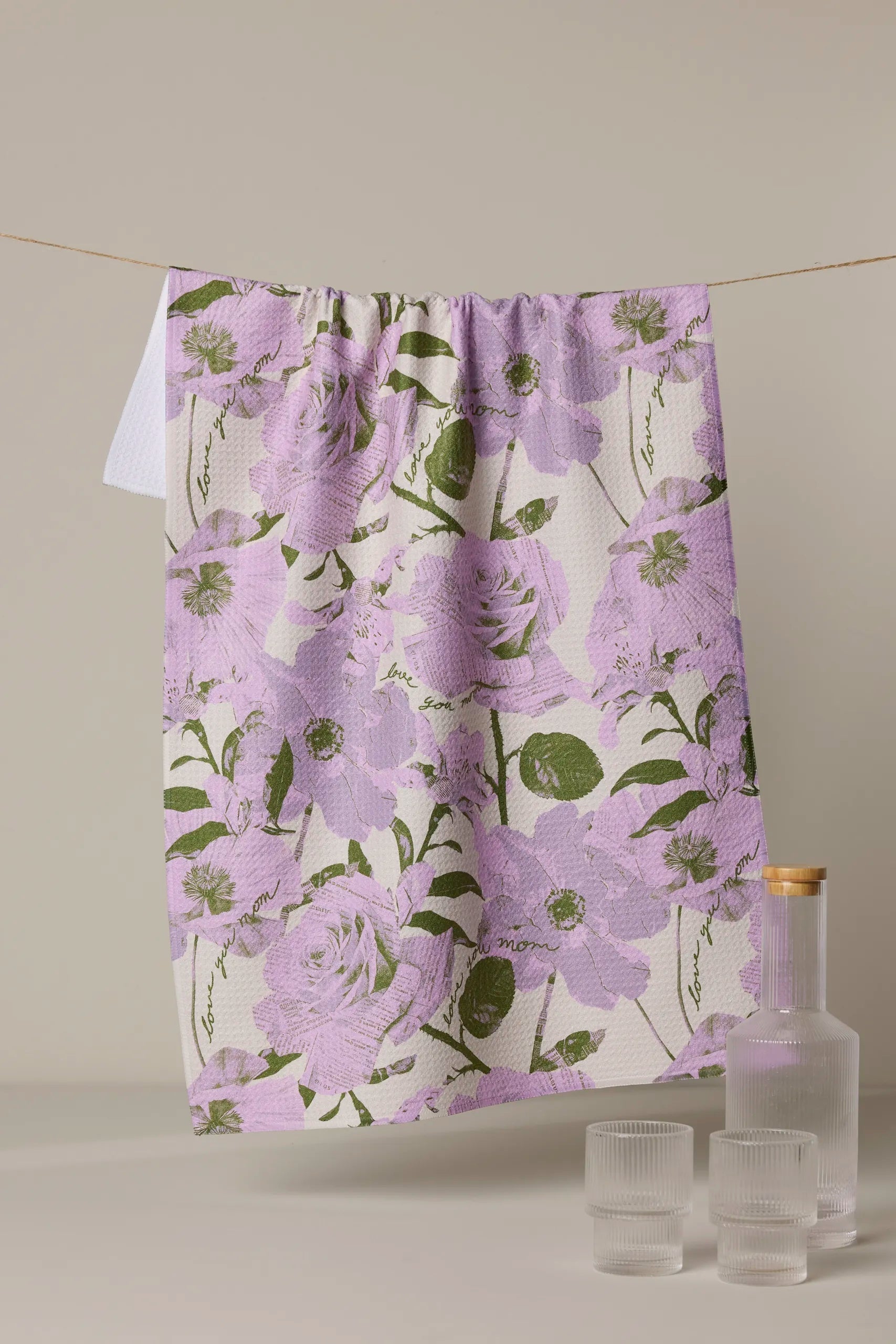 Floral patterned towel hanging on a line with a bottle and glasses below.