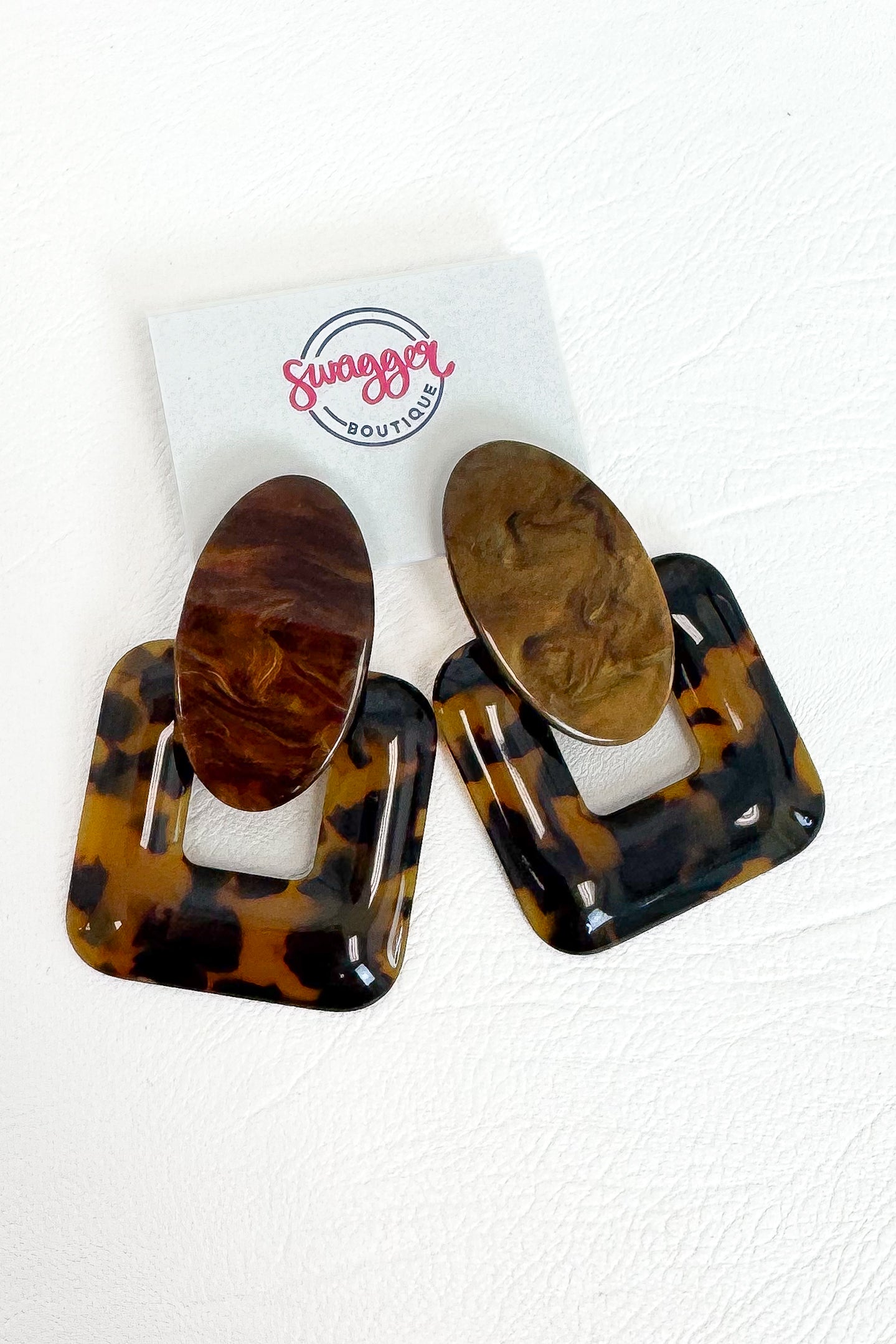 A pair of large square and oval drop earrings in glossy tortoiseshell and wood-grain patterns, displayed on a white card with the &