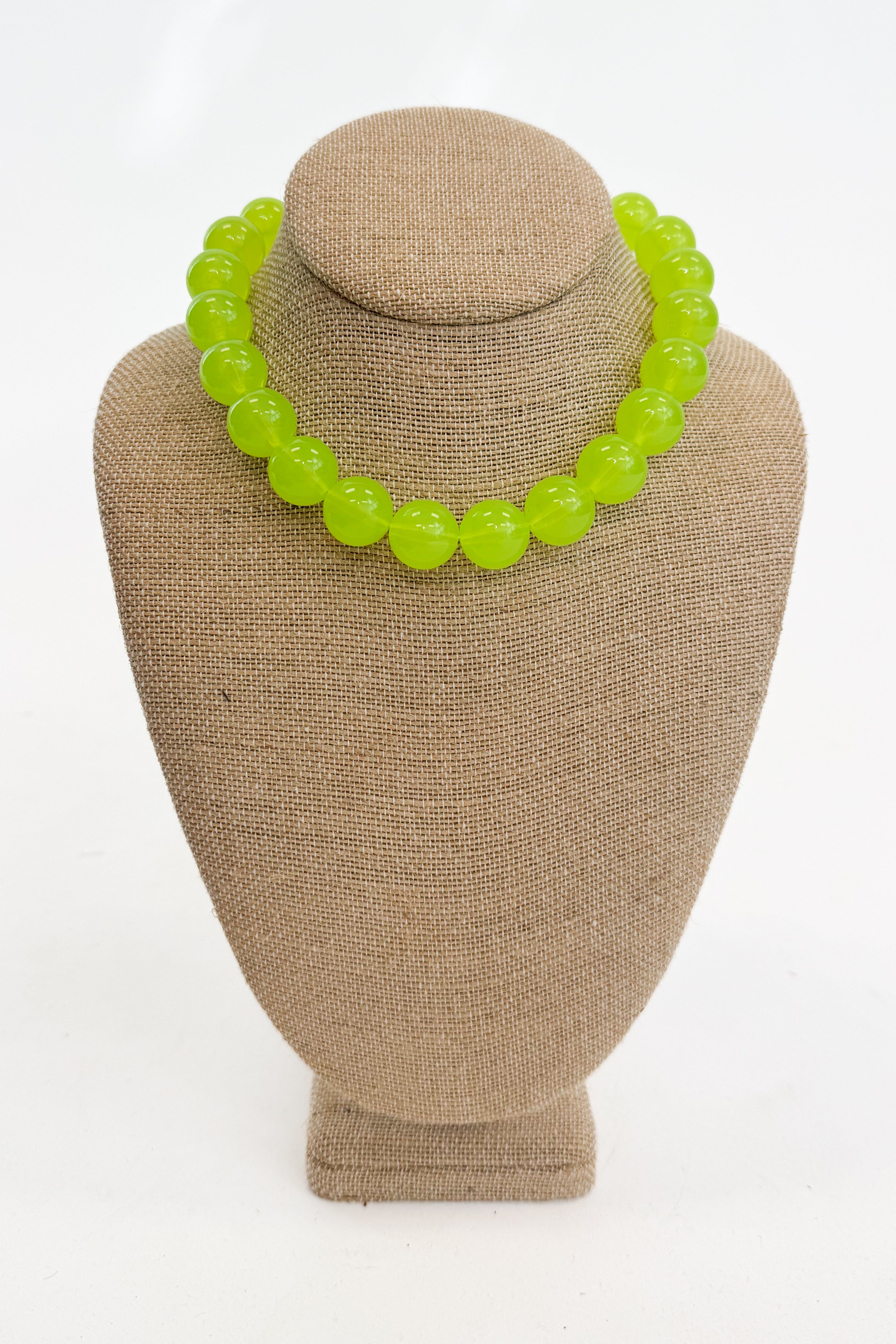 Neon green beaded necklace on a beige mannequin bust against a white background