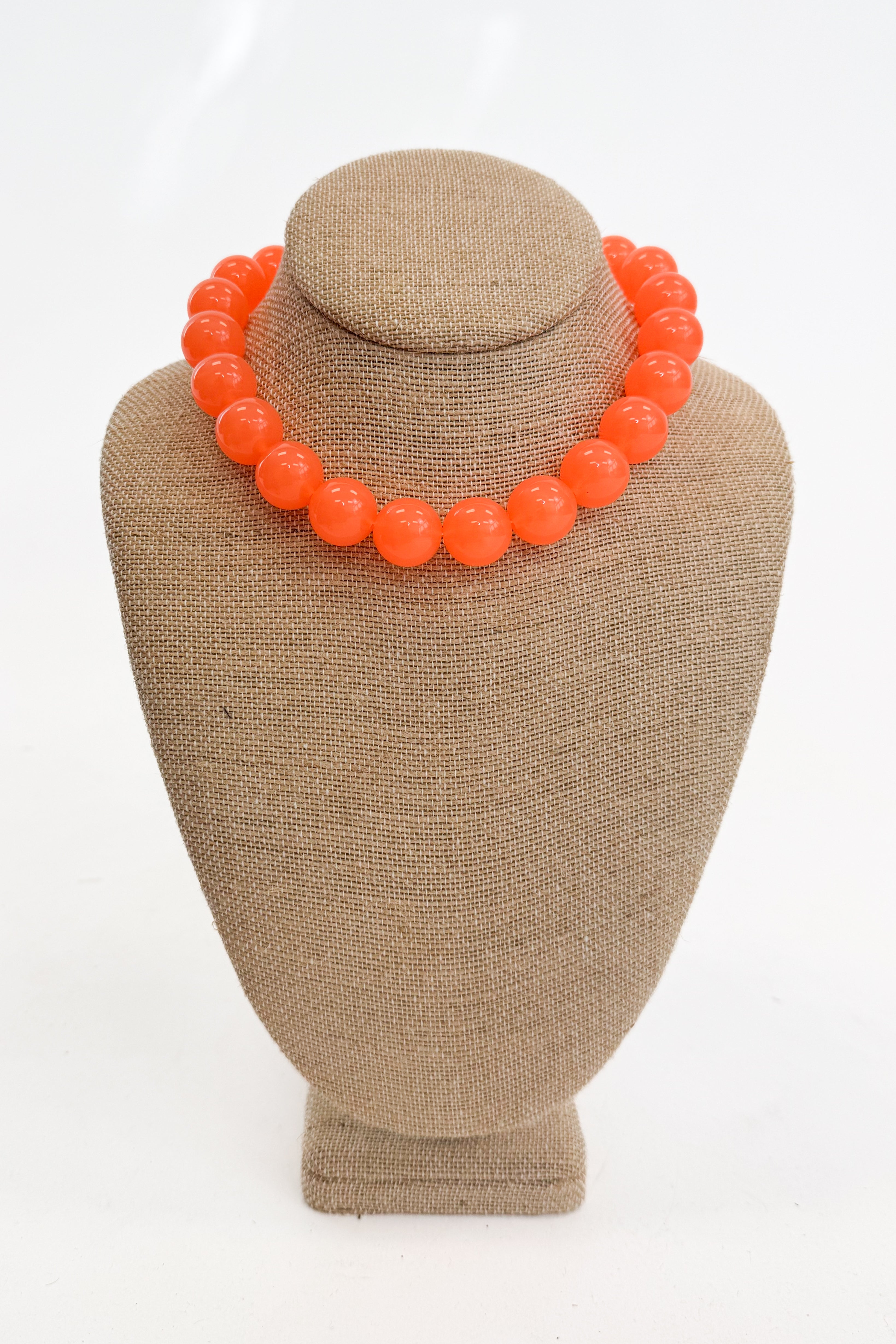 Neon orange beaded necklace on a brown mannequin bust against a white background