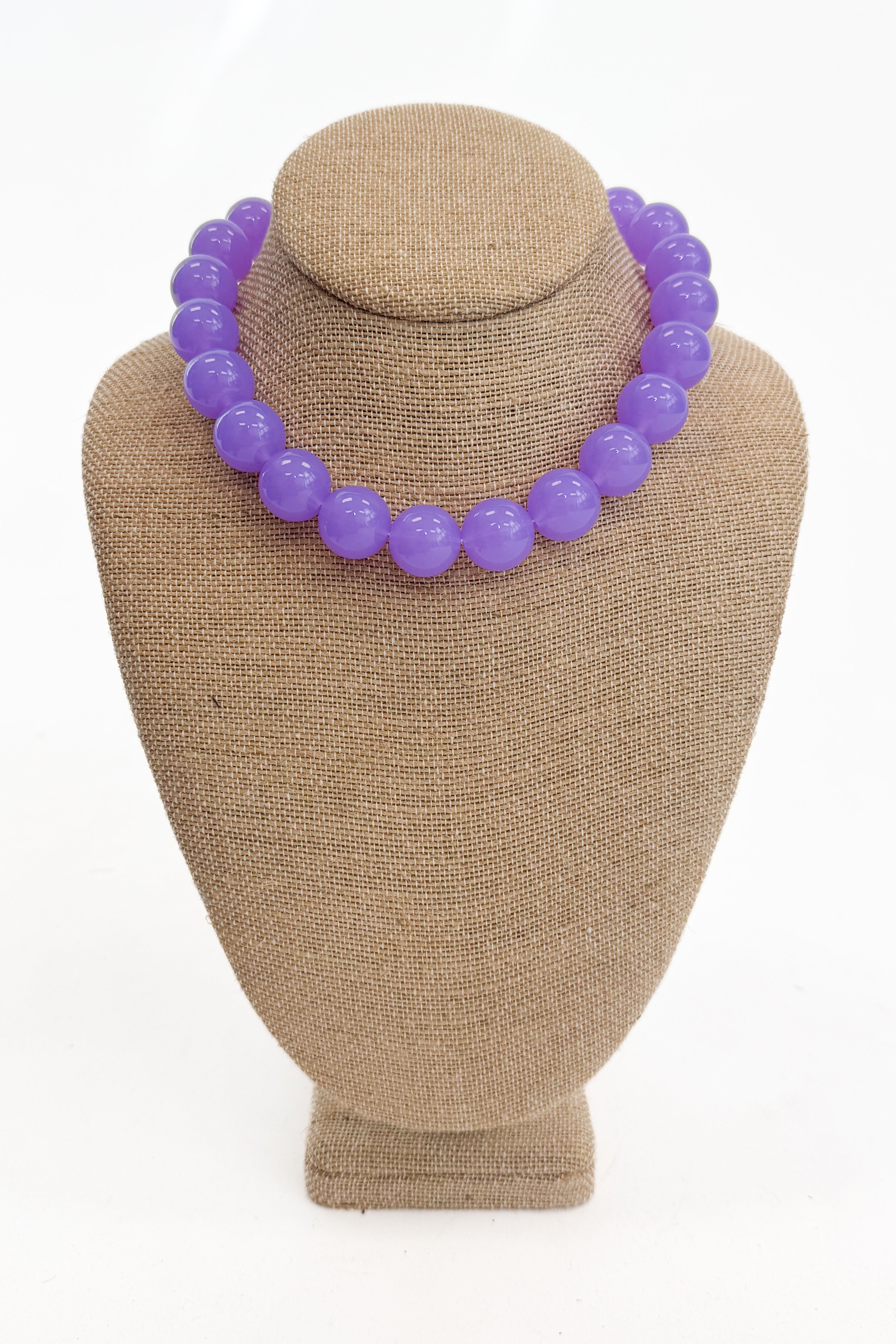 Purple beaded necklace on a brown mannequin bust against a white background