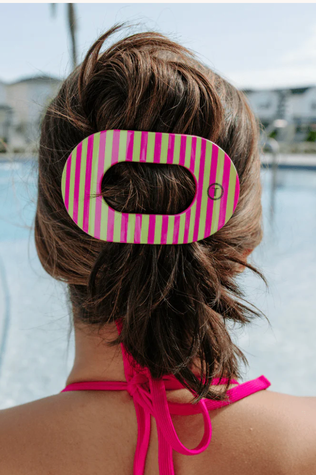 Person with a pink and green striped hair clip in their bun by a pool.