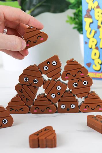 Stack of brown poop-shaped pieces with facial expressions on a white surface, with a hand holding one above them.