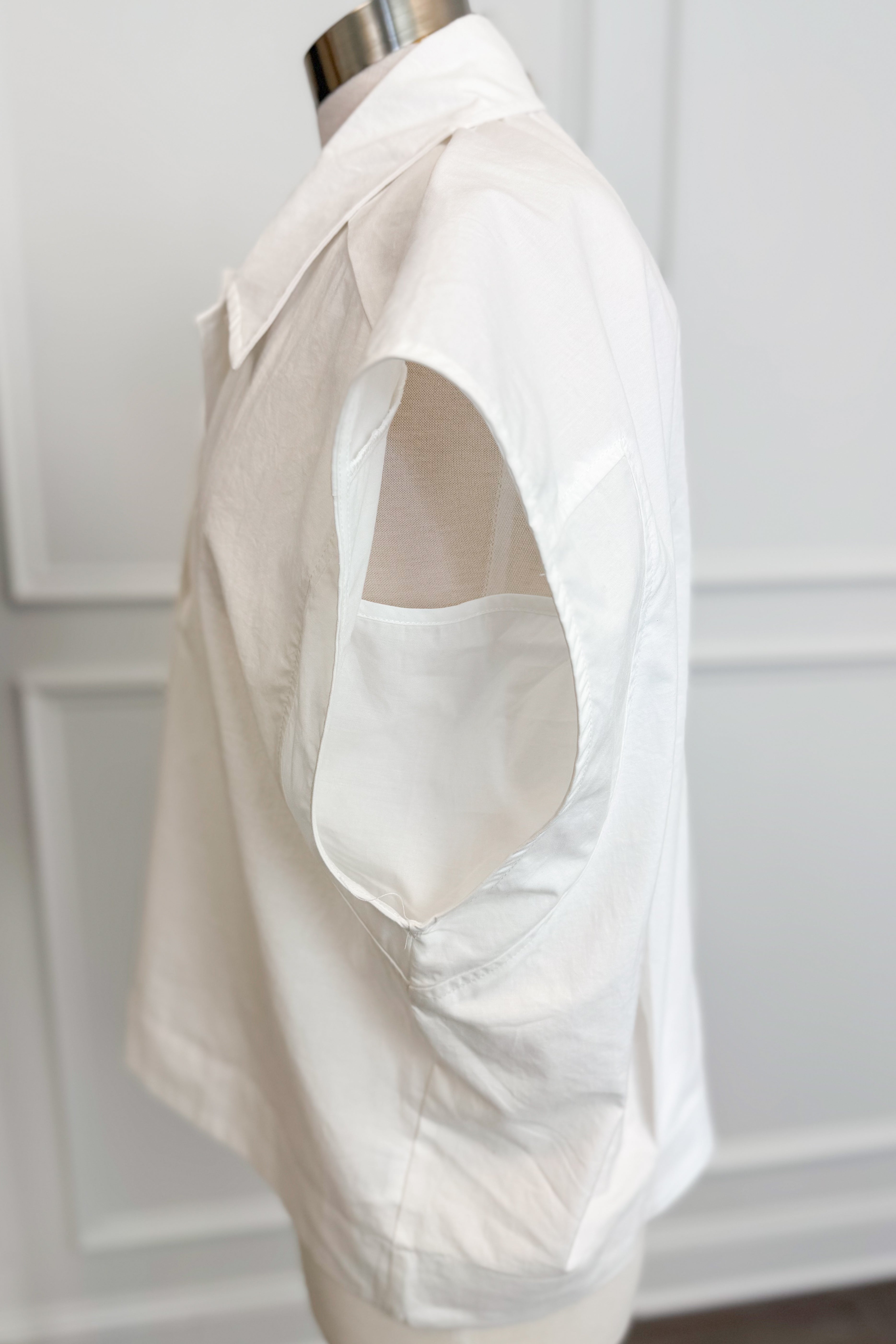 White sleeveless shirt on a mannequin against a white paneled wall.