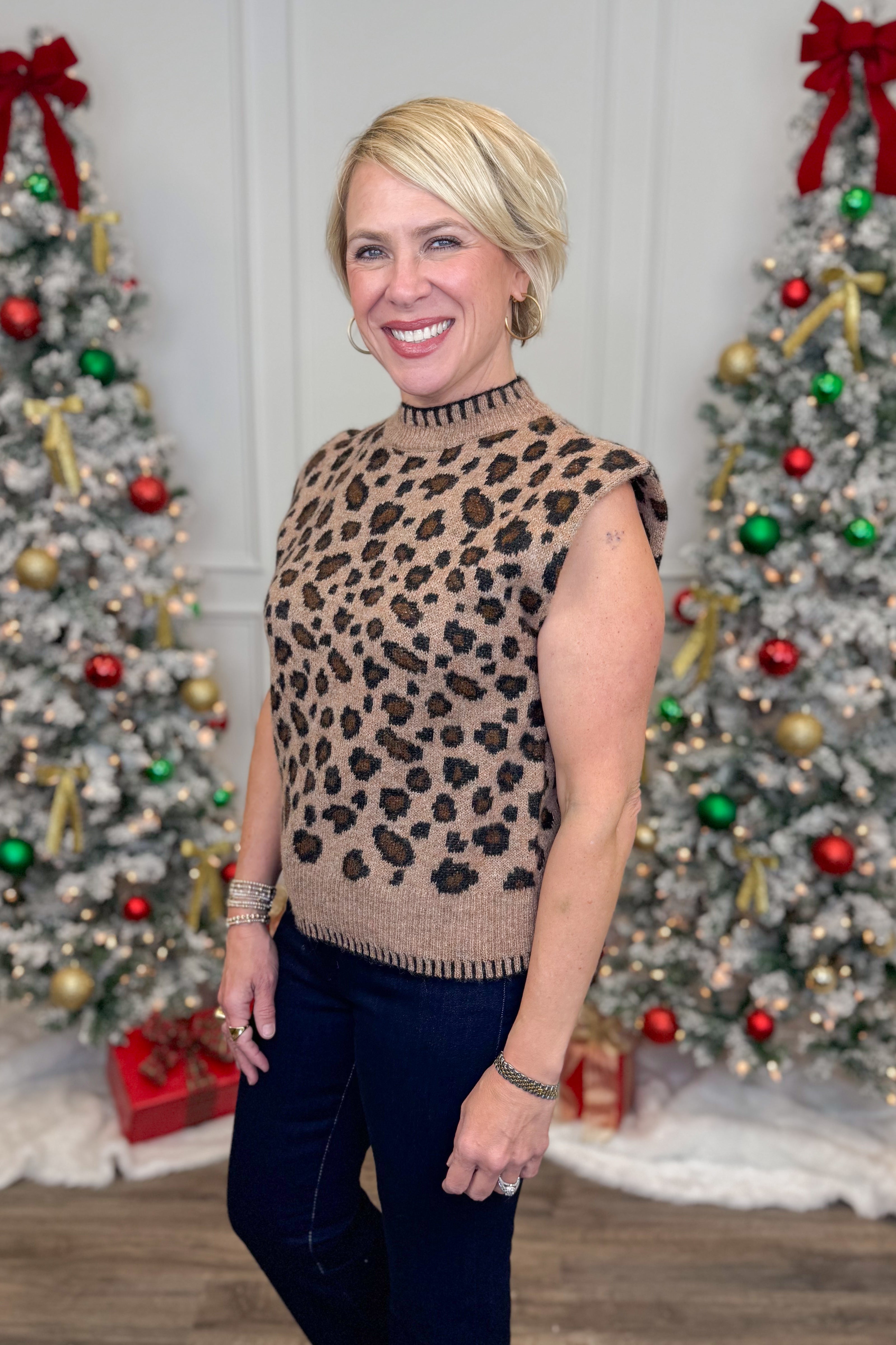 Woman wearing a leopard print sweater in front of Christmas trees