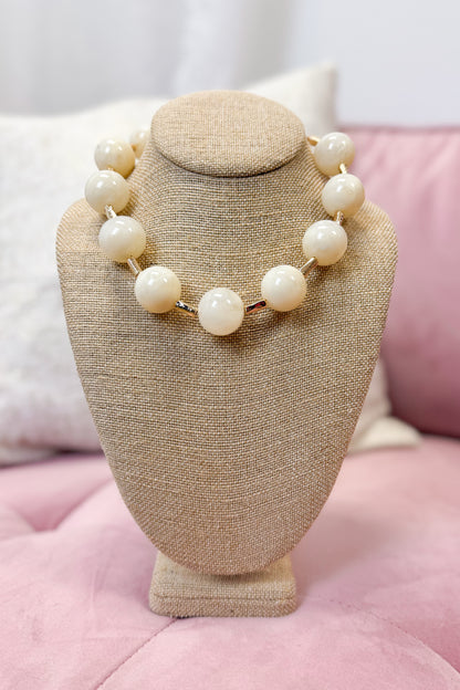 Necklace on a beige jewelry stand with a pink cushion background