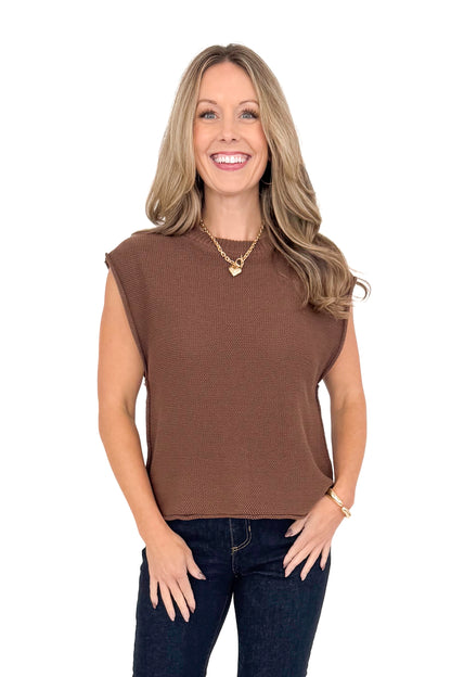 Front view of woman wearing brown sweater with jeans against white studio background.
