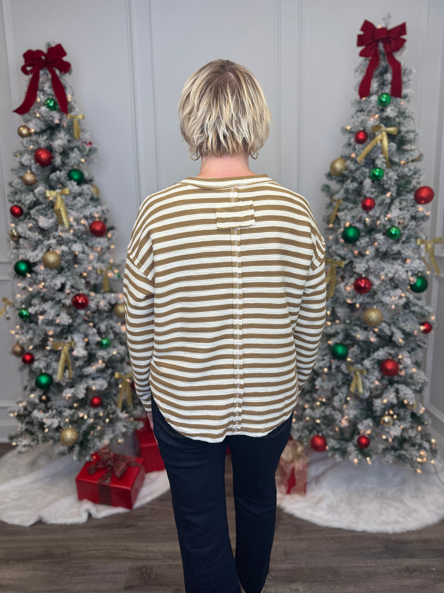 Person wearing a striped shirt standing in front of two decorated Christmas trees.