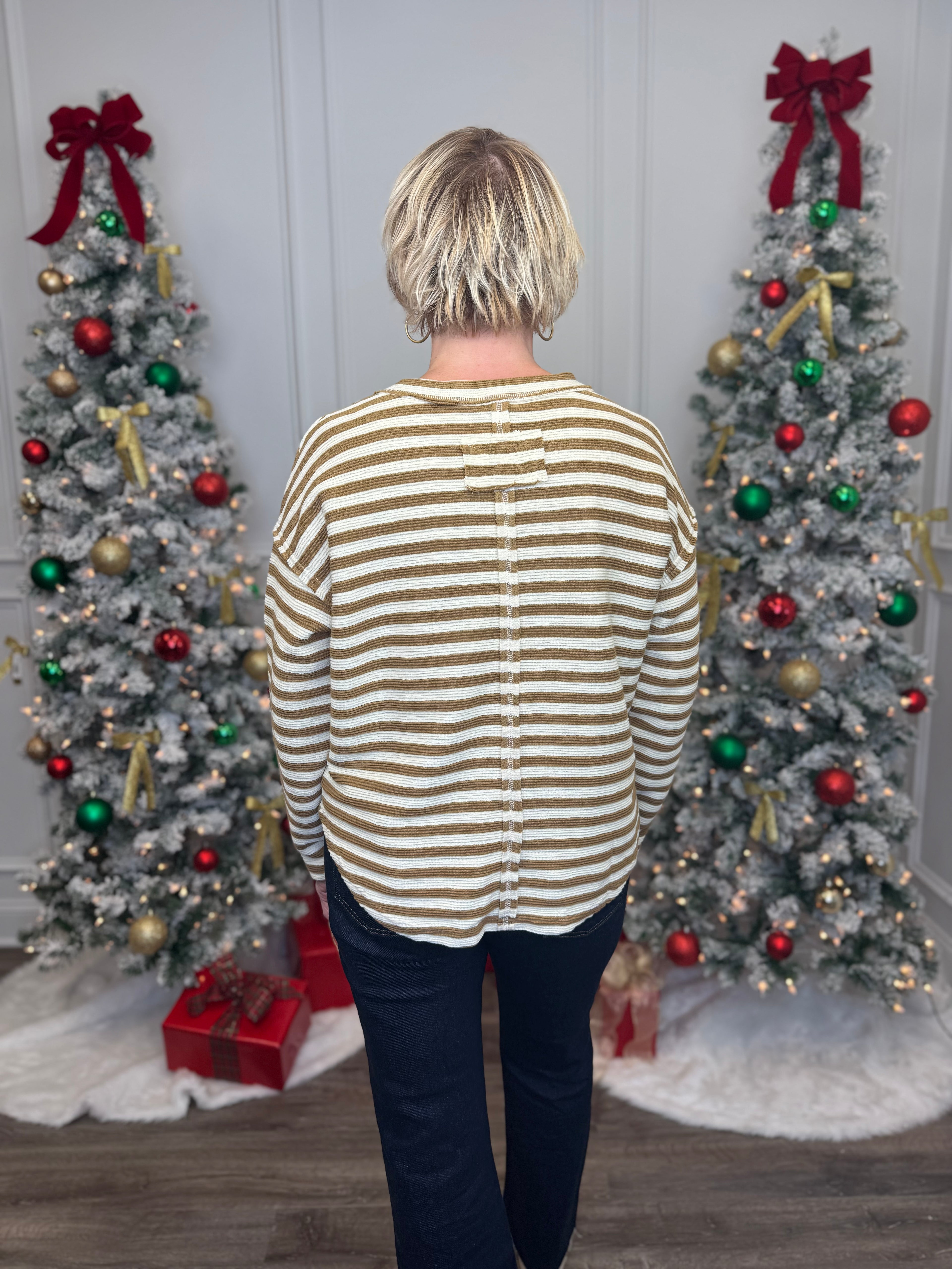 Person wearing a striped shirt standing in front of two decorated Christmas trees.
