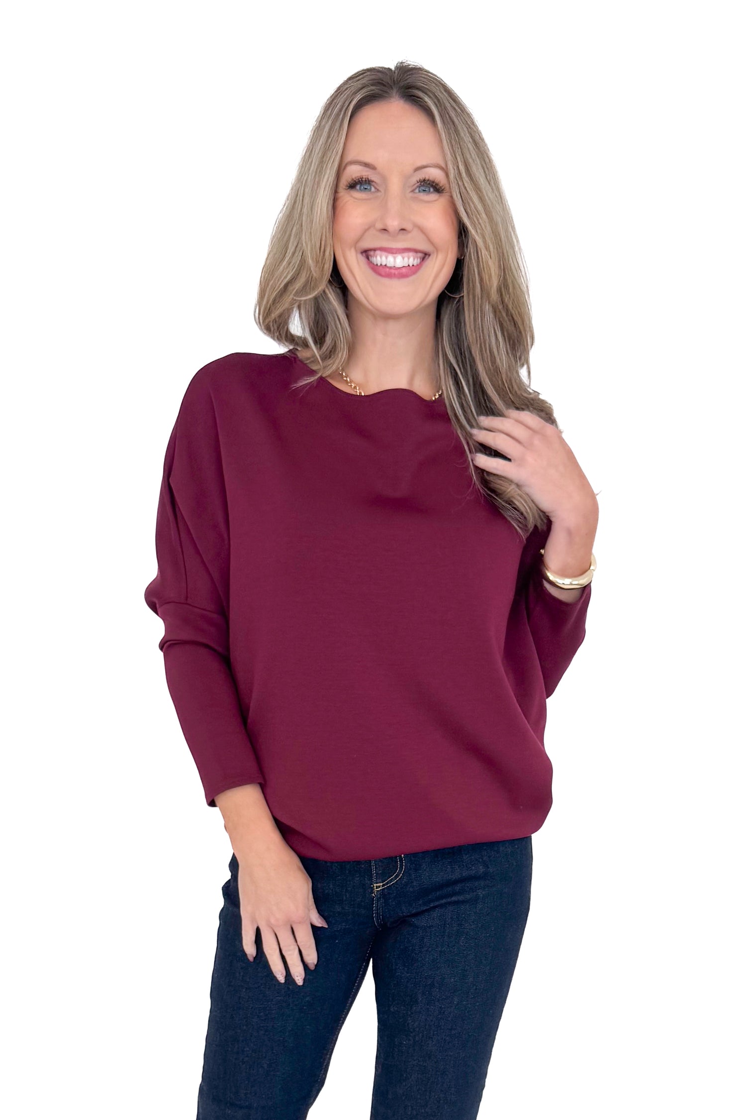 Front view of woman wearing burgundy top with jeans against white studio background.