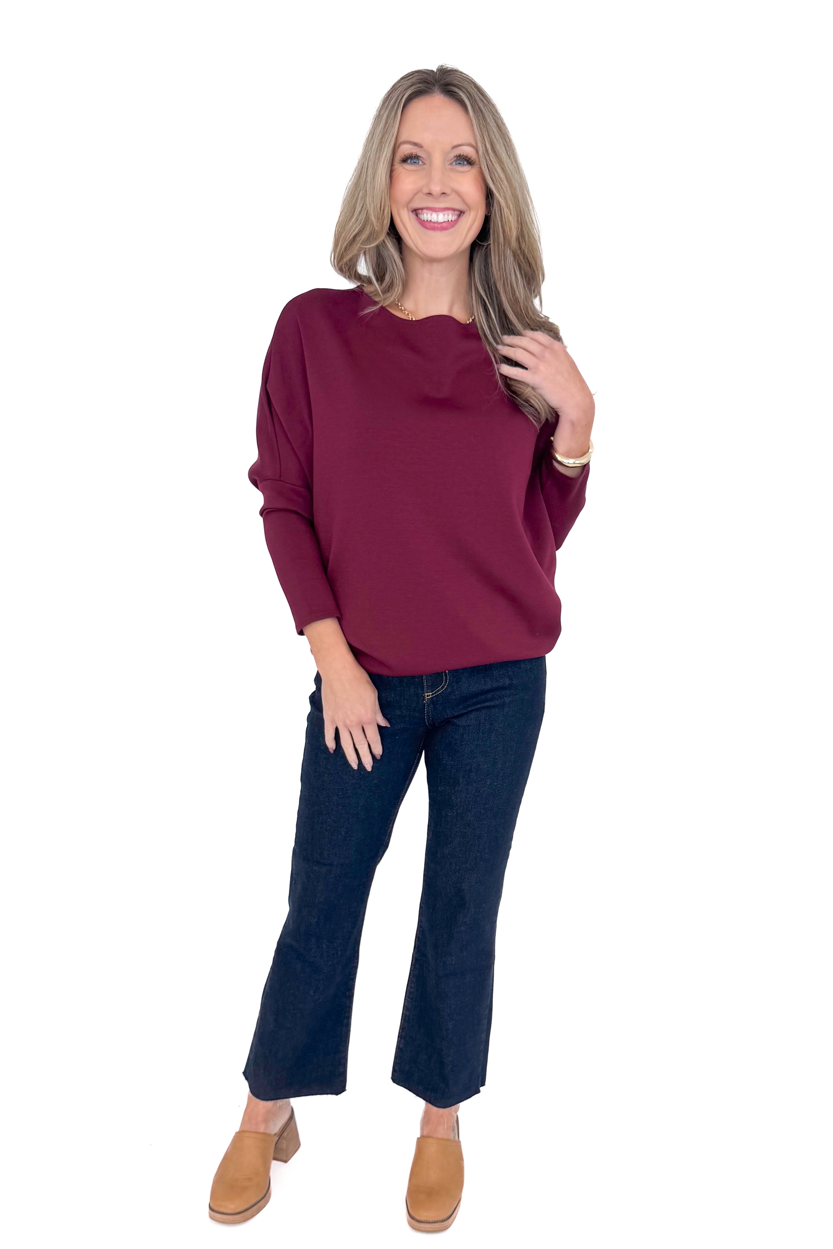 Front view of woman wearing burgundy top with jeans against white studio background.