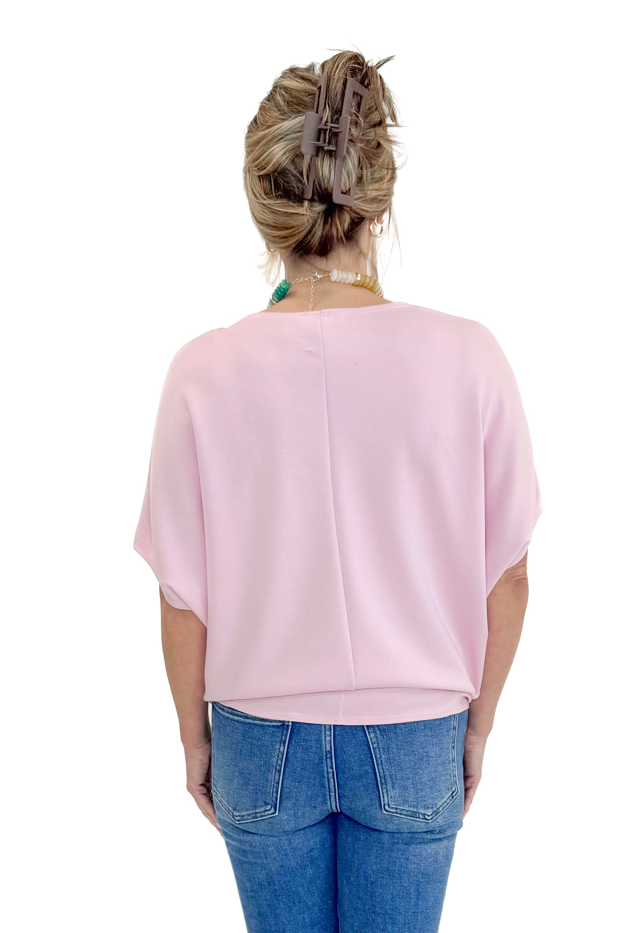 Back view of woman wearing Light Pink Dolman Sleeve Top with jeans against white studio background.