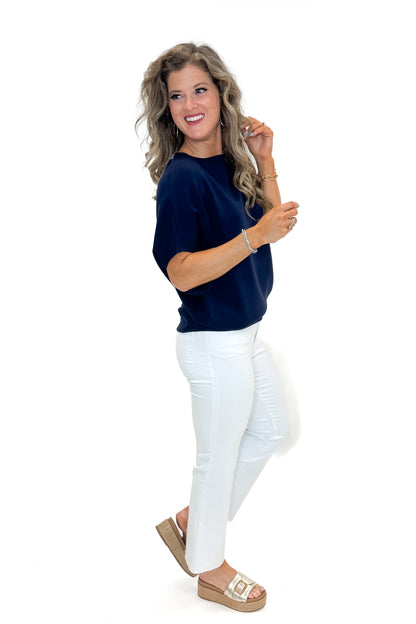 Side view of woman wearing Navy Dolman Sleeve Top with jeans against white studio background.