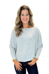 Front view of woman wearing Grey Ribbed Dolman Sleeve Top with jeans against white studio background.