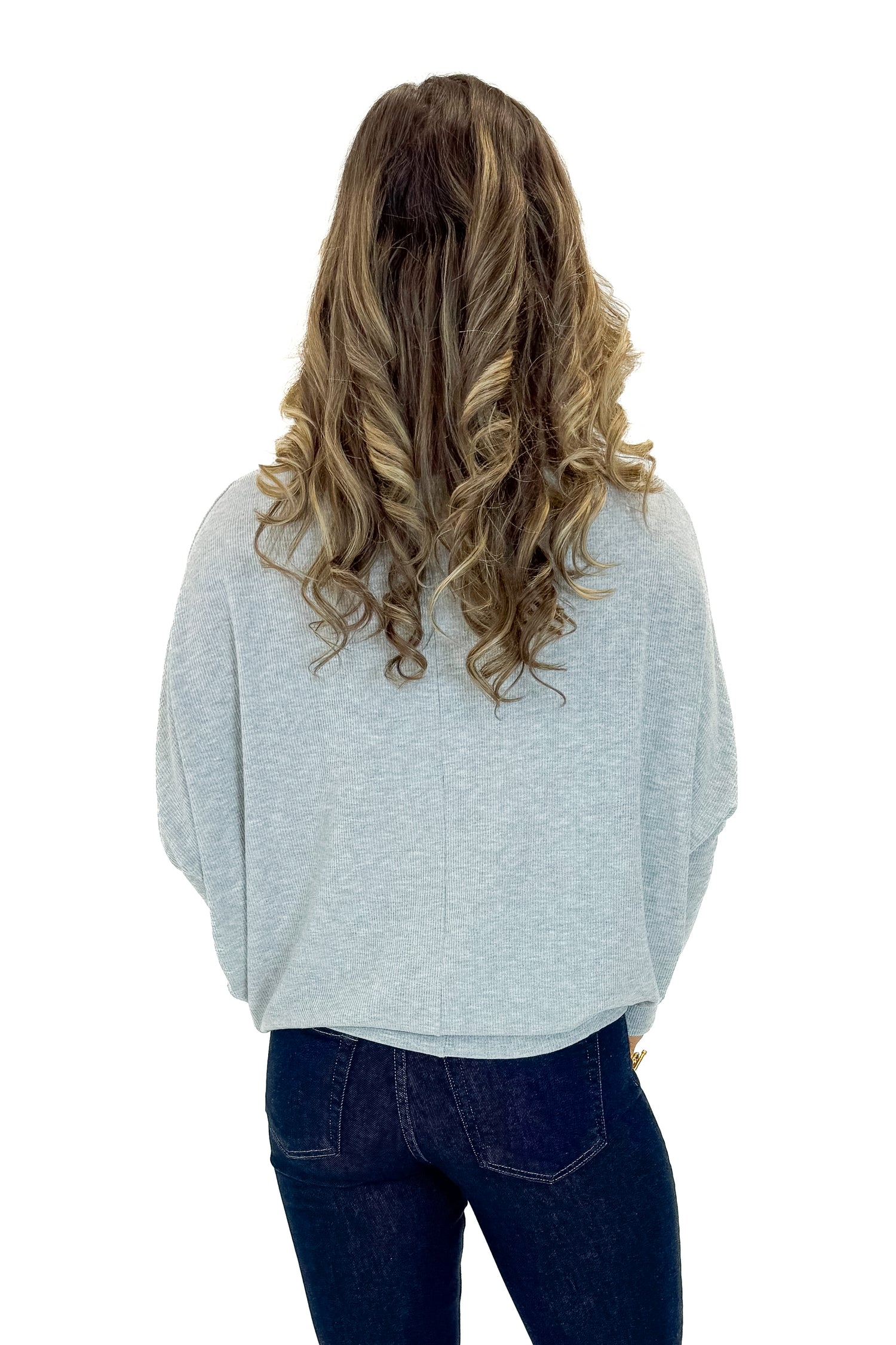 Back view of woman wearing Grey Ribbed Dolman Sleeve Top with jeans against white studio background.