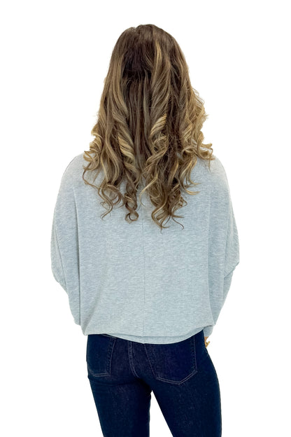 Back view of woman wearing Grey Ribbed Dolman Sleeve Top with jeans against white studio background.