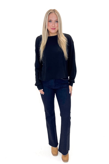 Front view of woman wearing Black Open Back Top with jeans against white studio background.