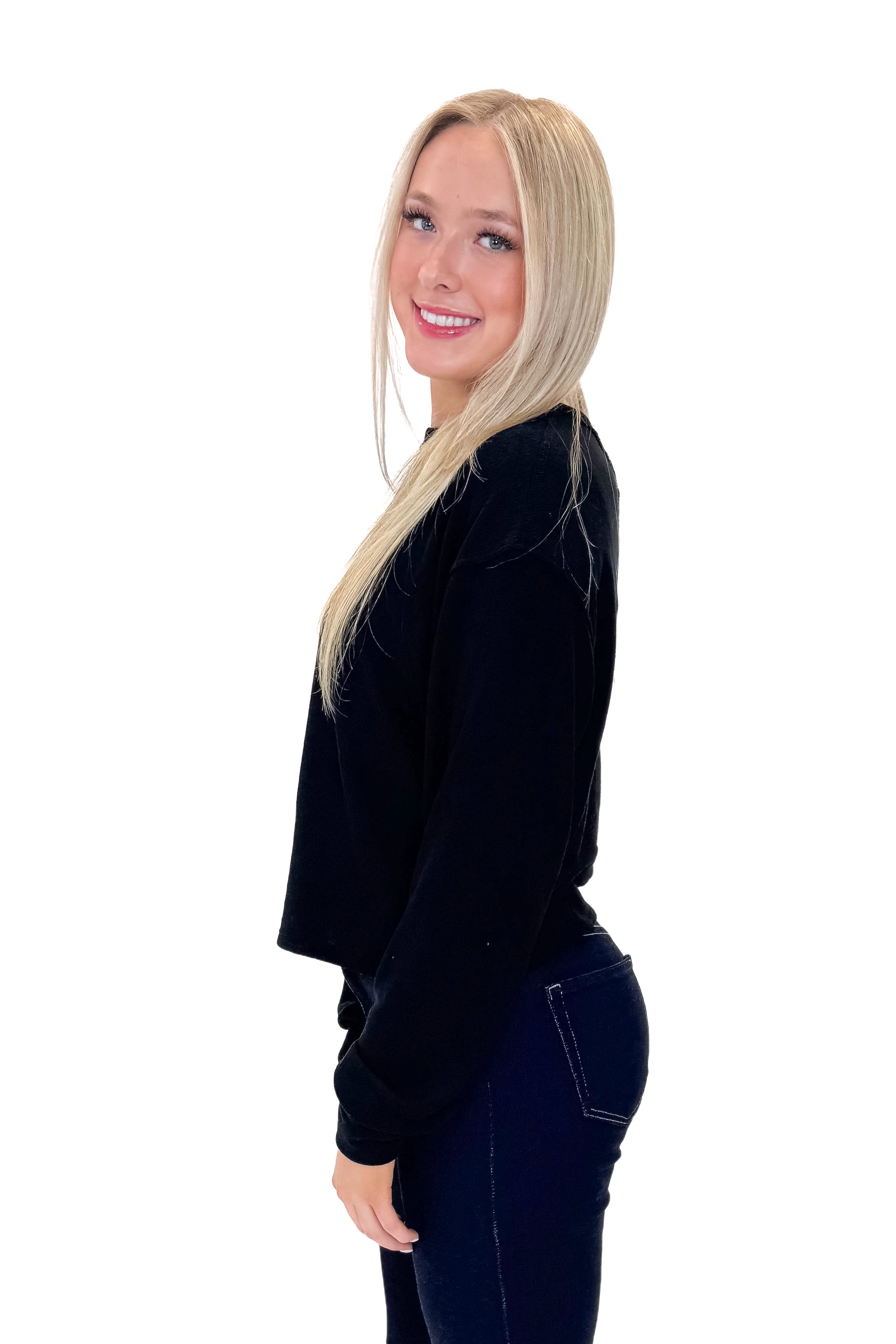 Side view of woman wearing Black Open Back Top with jeans against white studio background.