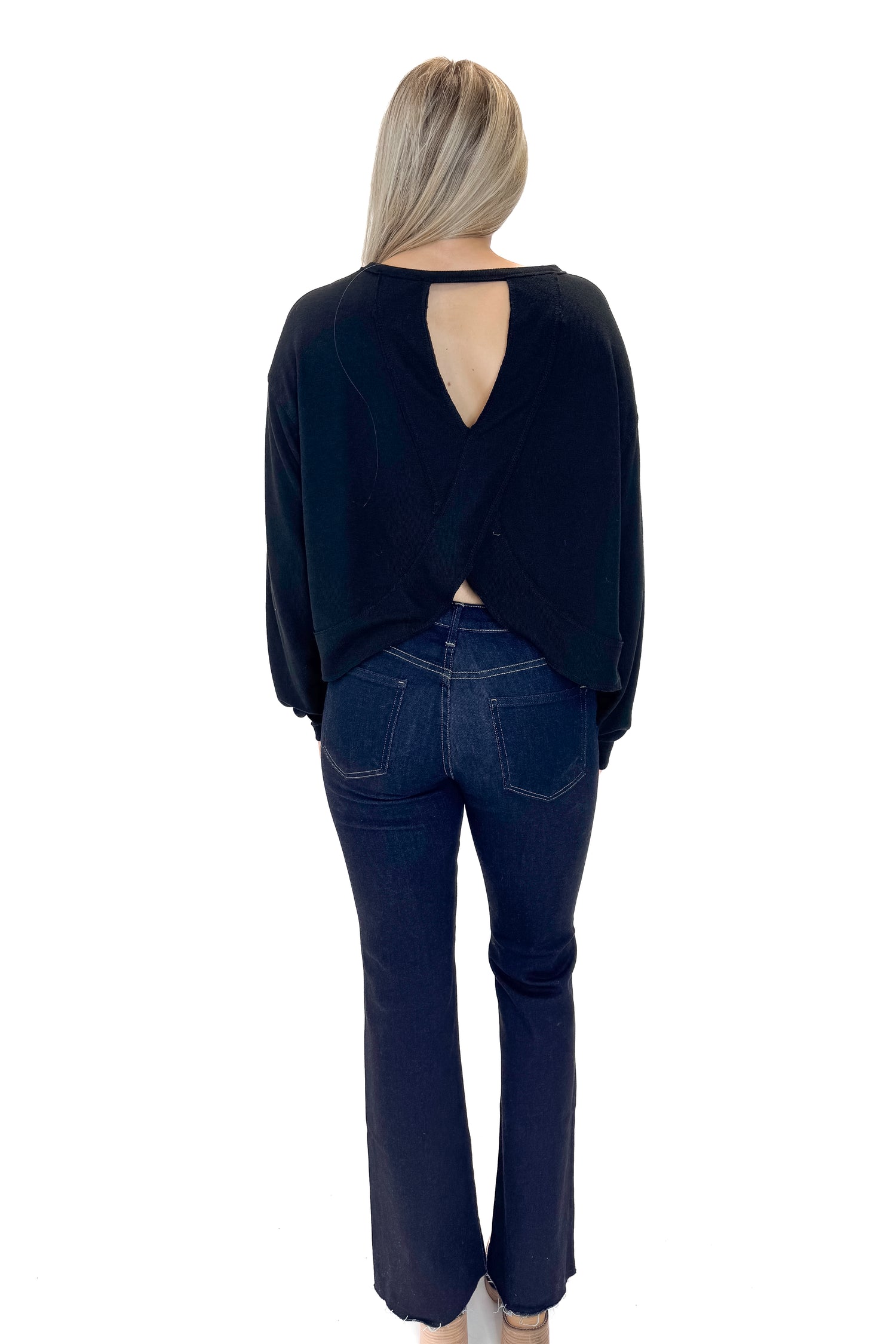 Back view of woman wearing Black Open Back Top with jeans against white studio background.
