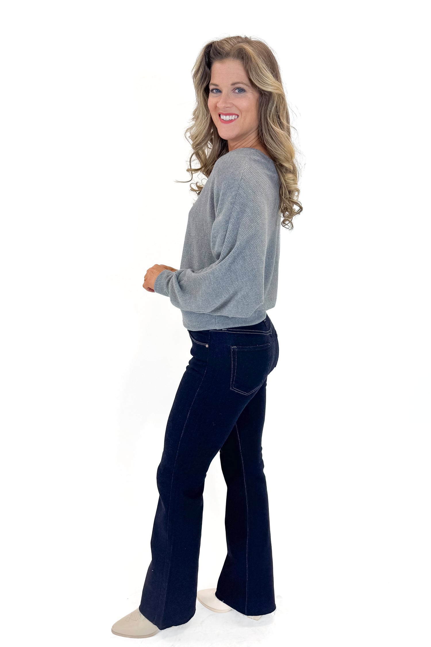 Side view of woman wearing Heather Grey Ribbed V-neck Banded Top with jeans against white studio background.