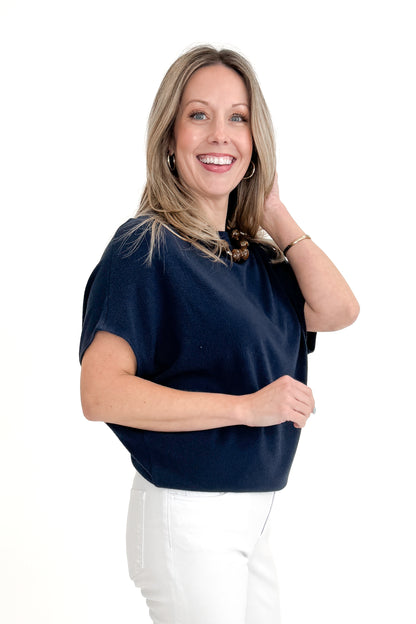 Side view of woman wearing Navy Dolman Sleeve Cocoon Top with jeans against white studio background.