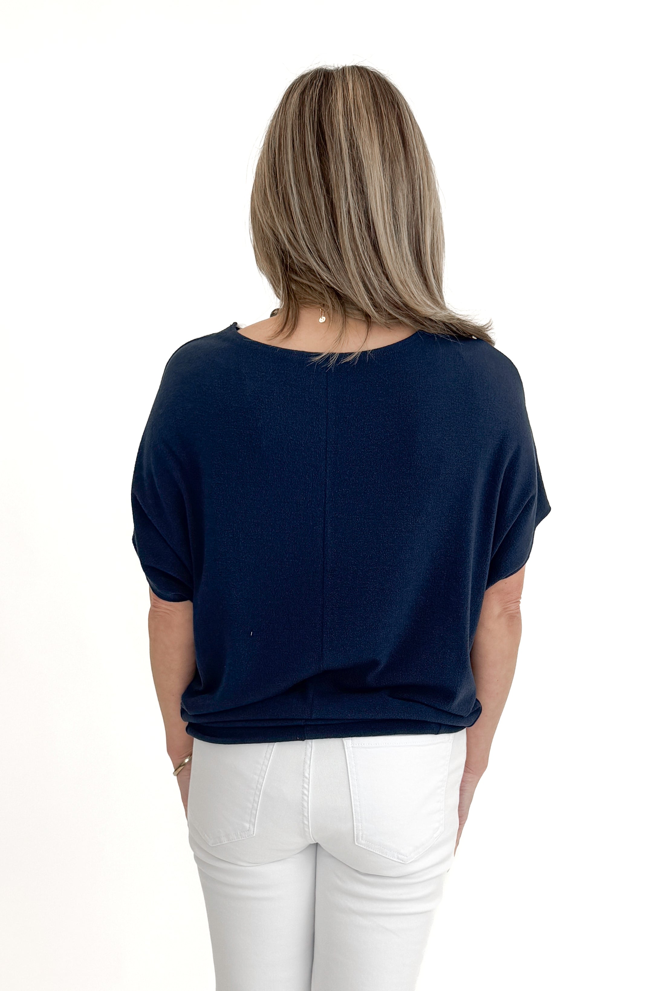 Back view of woman wearing Navy Dolman Sleeve Cocoon Top with jeans against white studio background.
