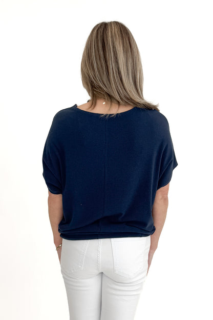 Back view of woman wearing Navy Dolman Sleeve Cocoon Top with jeans against white studio background.