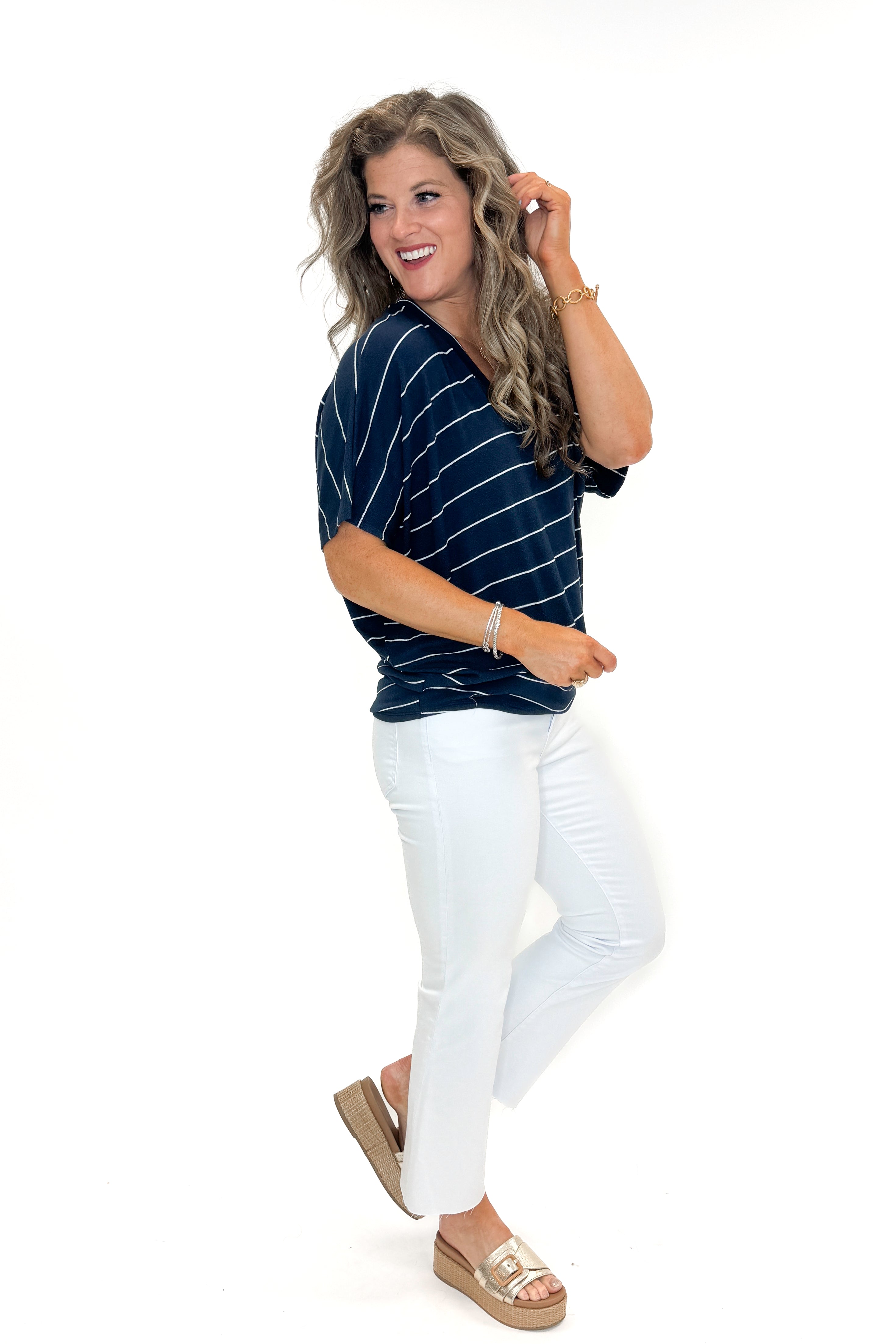 Side view of woman wearing Navy Striped Cocoon Top with jeans against white studio background.