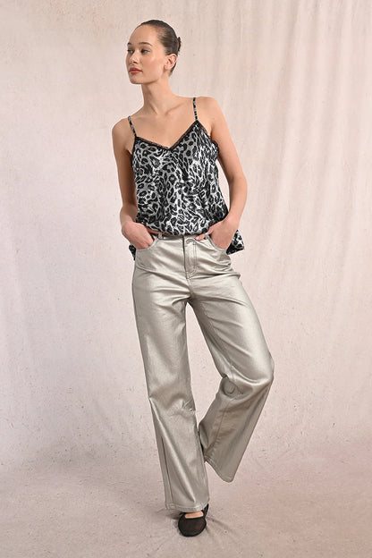 Front view of woman wearing silver coated jeans and black top against tan studio background.