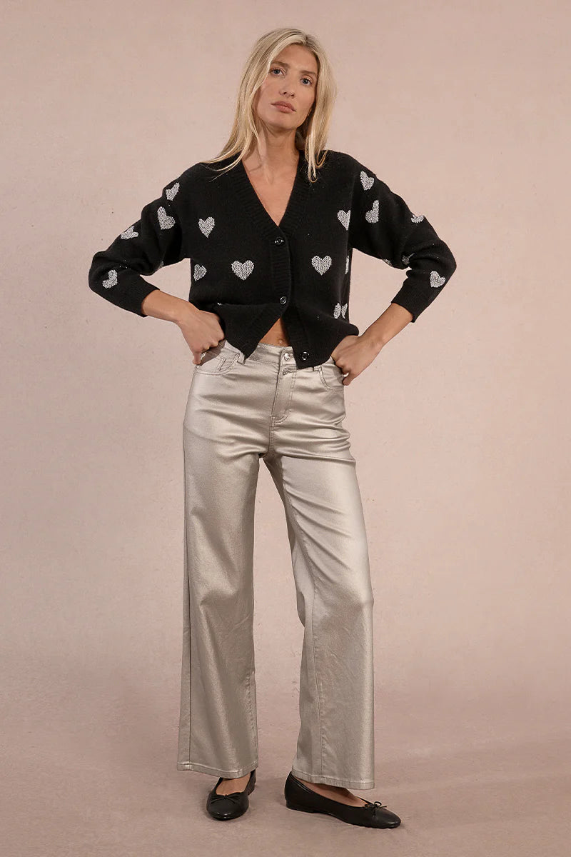 Front view of woman wearing silver coated jeans and black top against tan studio background.