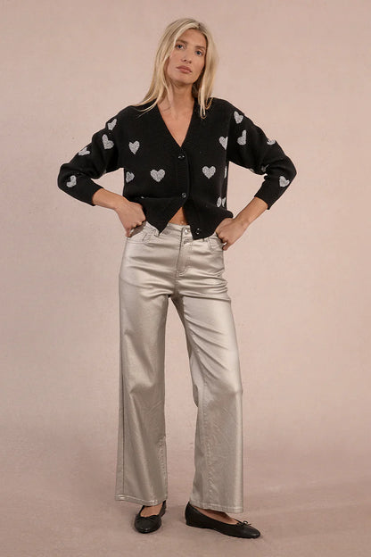 Front view of woman wearing silver coated jeans and black top against tan studio background.