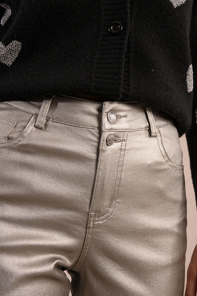 Front detailed view of woman wearing silver coated jeans and black top against tan studio background.
