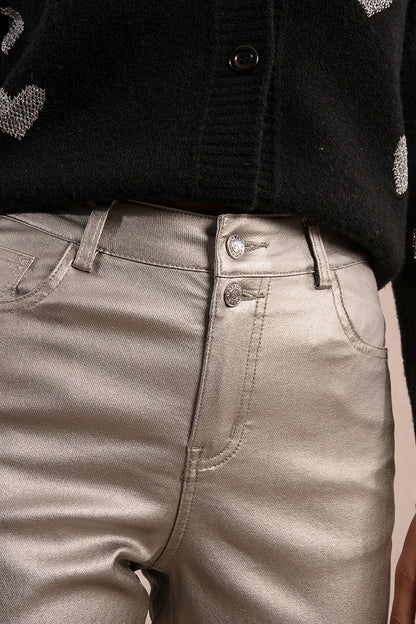 Front detailed view of woman wearing silver coated jeans and black top against tan studio background.