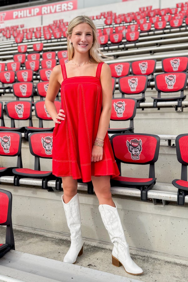 Woman in a red dress and white boots standing in front of stadium seats with logos.