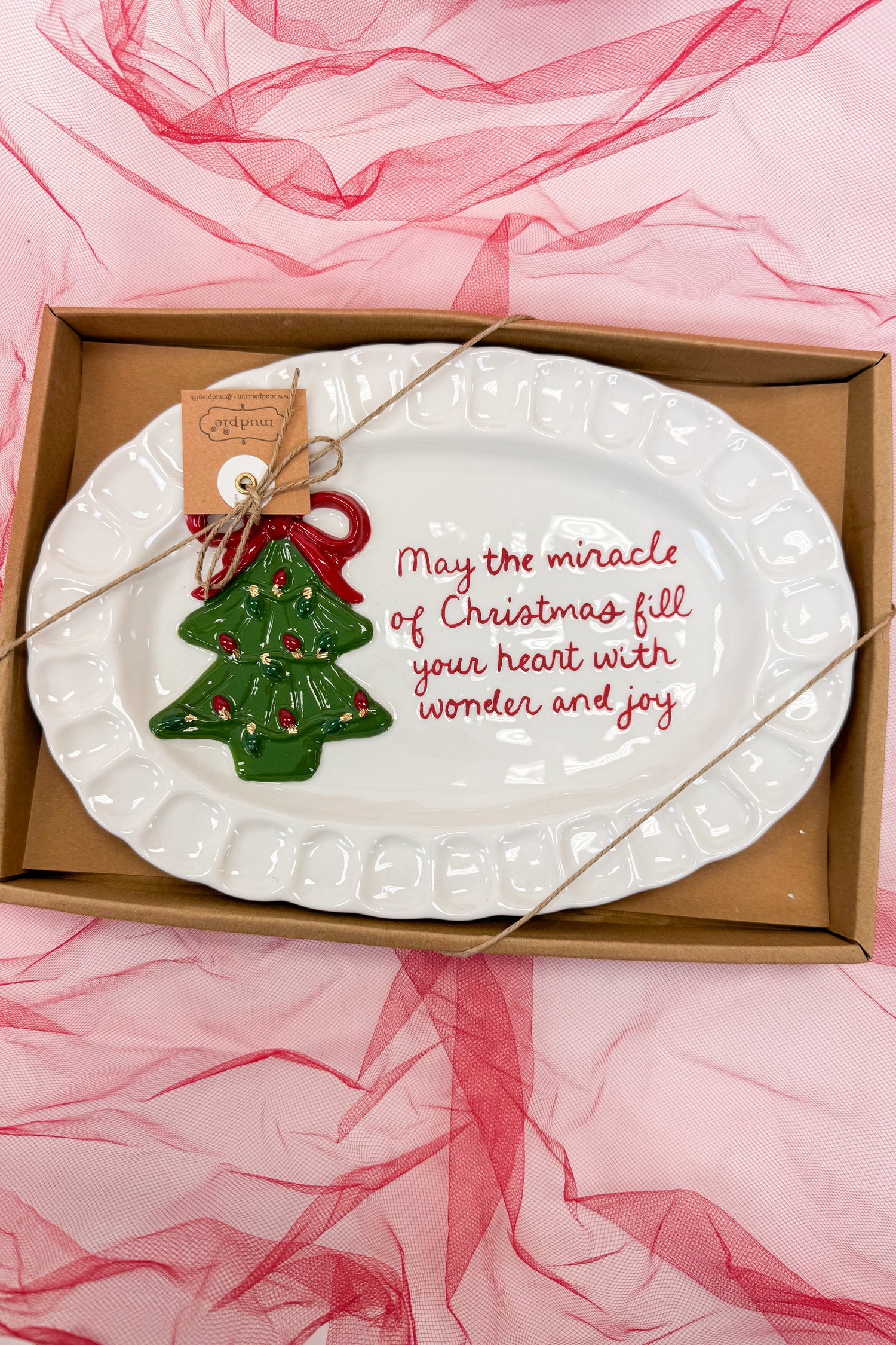 Decorative plate with Christmas tree ornament and text in a box on pink fabric background