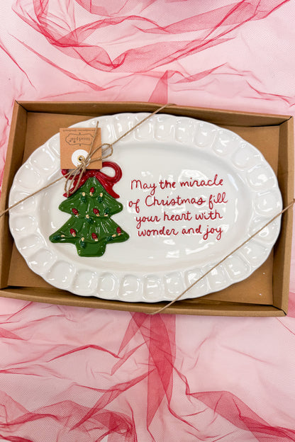 Decorative plate with Christmas tree ornament and text in a box on pink fabric background