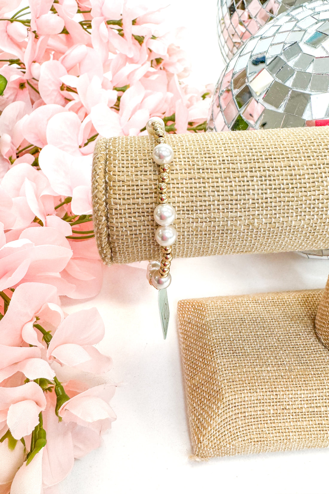 beaded bracelet with pearl detailing on a white surface with pink flowers in the background