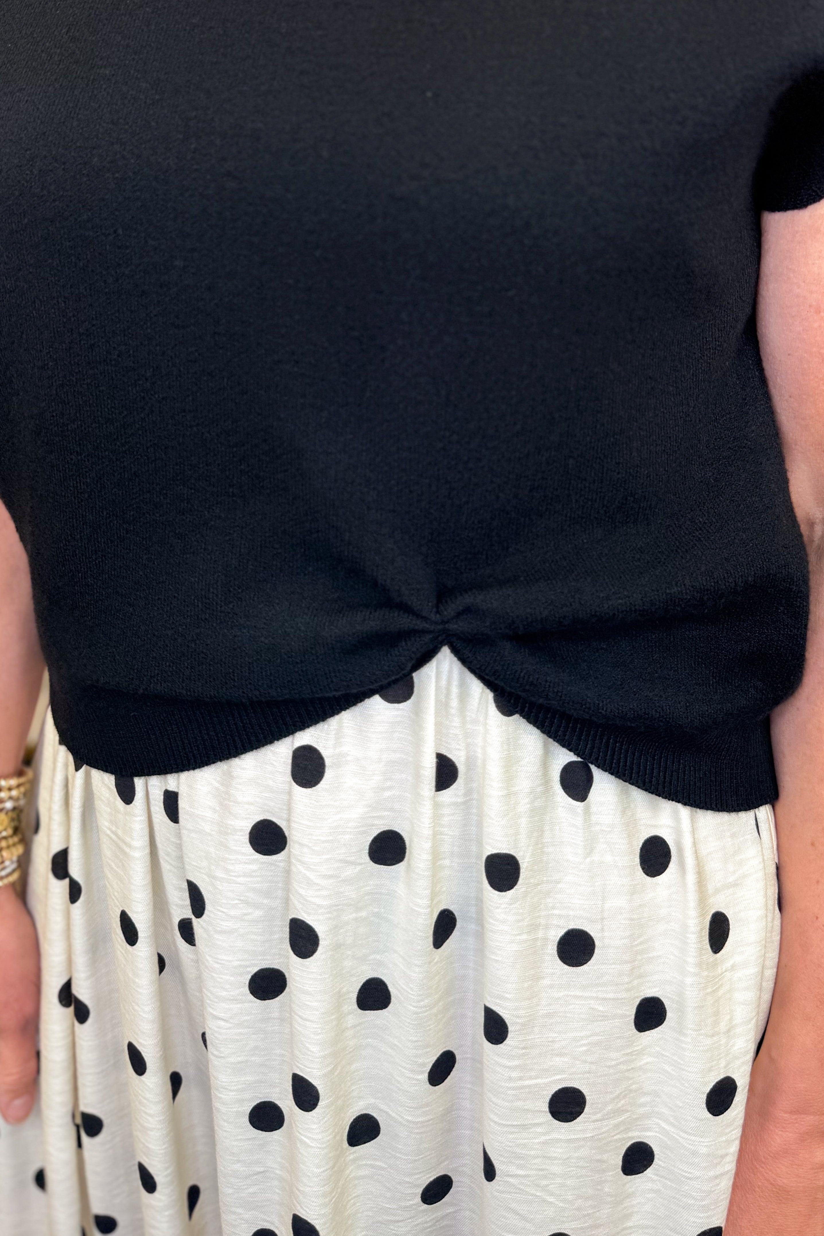 Front detail view of woman wearing Swagger Boutique’s Black &amp; Cream Polka Dot Layered Midi Dress by Entro with sandals at the store. 
