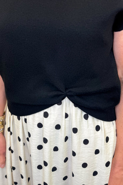 Front detail view of woman wearing Swagger Boutique’s Black &amp; Cream Polka Dot Layered Midi Dress by Entro with sandals at the store. 
