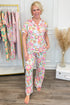 Woman wearing a floral pajama set standing in front of a rack with more pajamas.