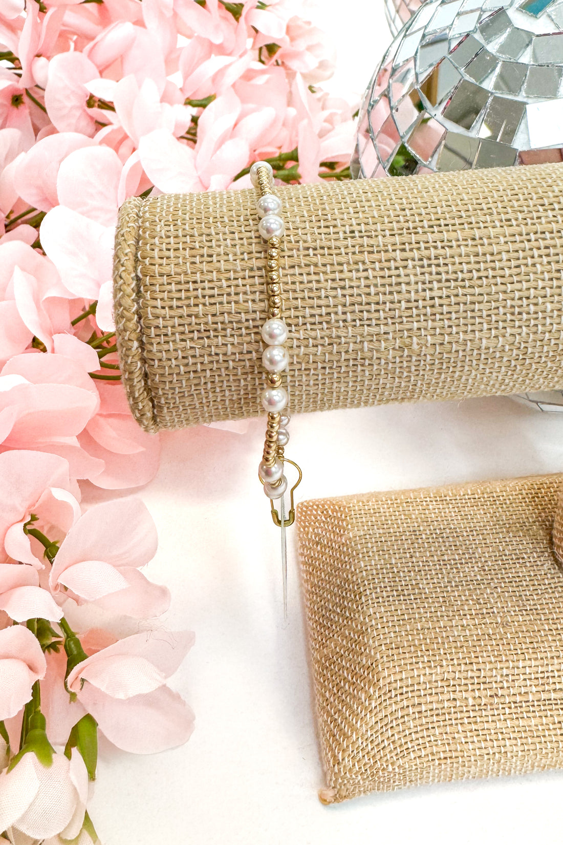 gold enewton bracelet with pearl detailing on burlap display with floral background