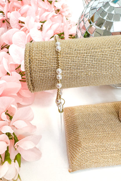 gold enewton bracelet with pearl detailing on burlap display with floral background