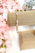 gold enewton bracelet with pearl detailing on burlap display with floral background