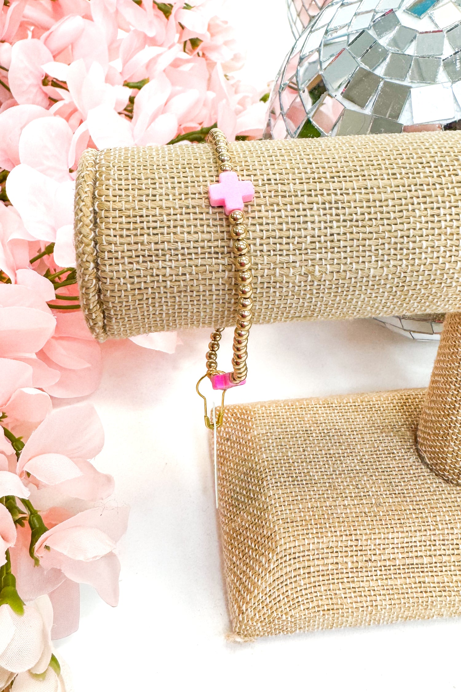 gold enewton bracelet with pink cross detailing  on burlap display with floral background