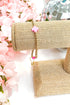 gold enewton bracelet with pink cross detailing  on burlap display with floral background