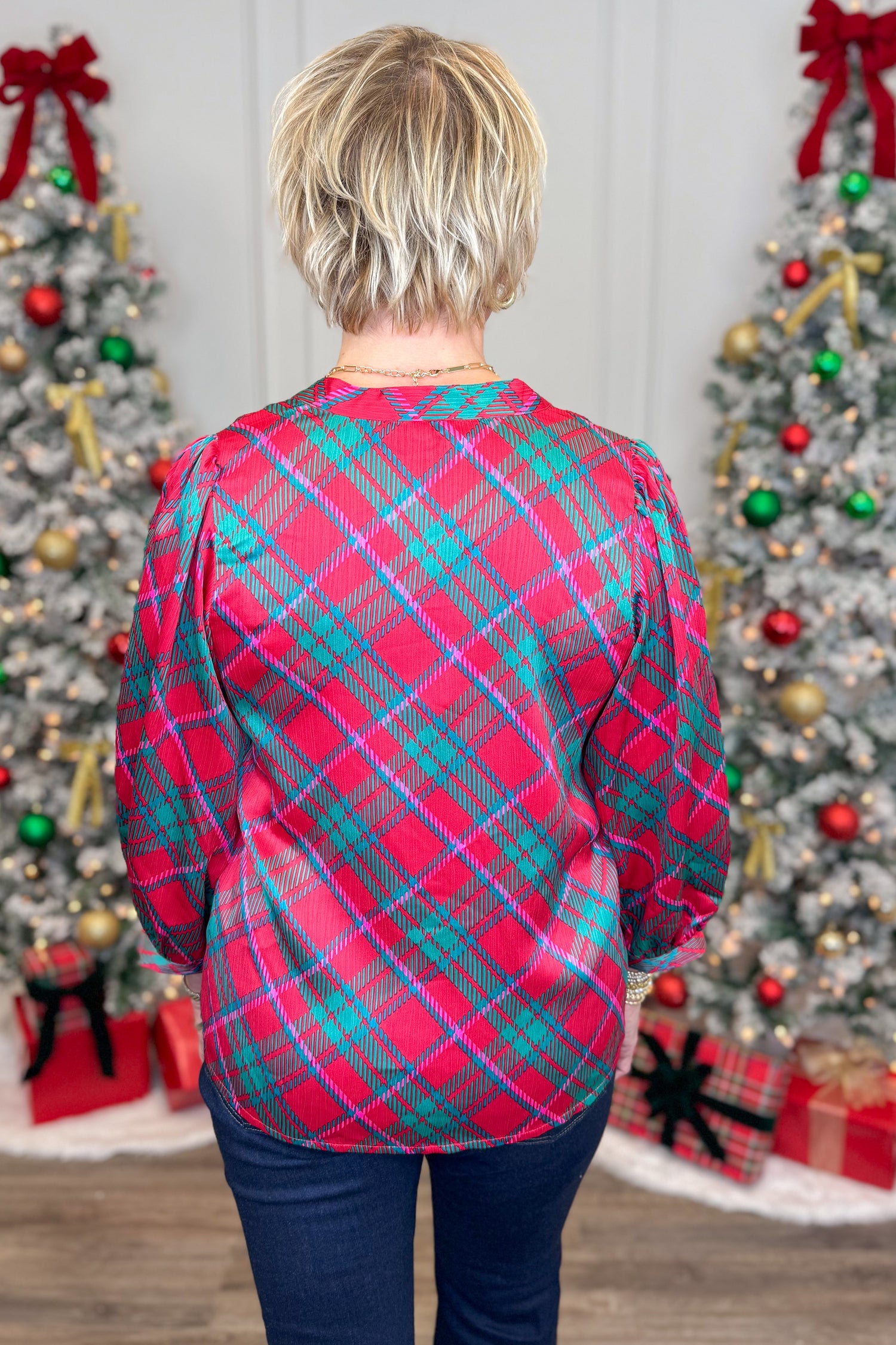 Person wearing a red and green plaid shirt with Christmas trees and decorations in the background
