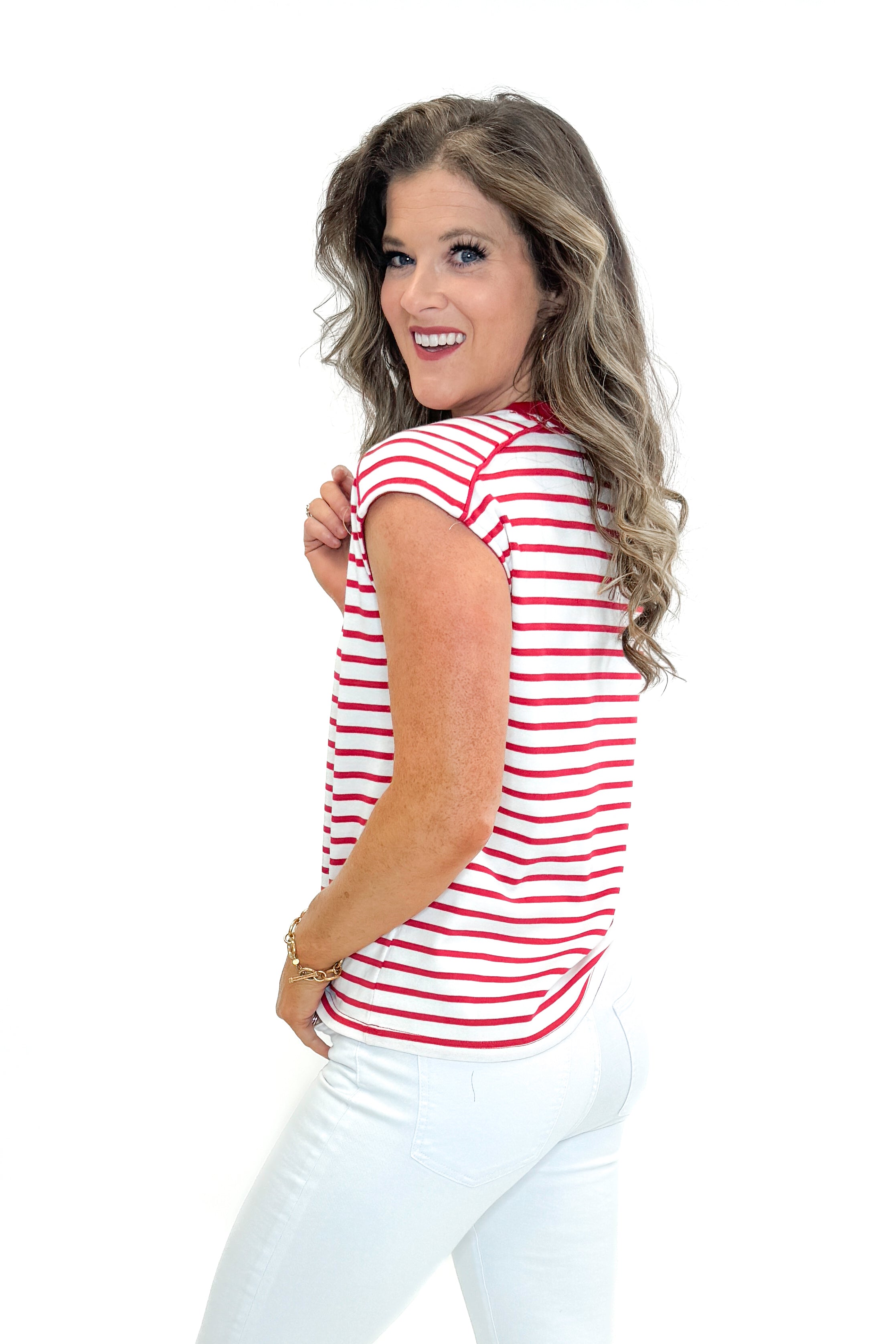 Side view of woman wearing Red Striped Sleeveless Top with white jeans against white studio background.