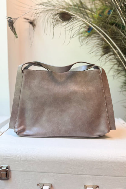 Gray leather handbag on a white surface with peacock feathers in the background