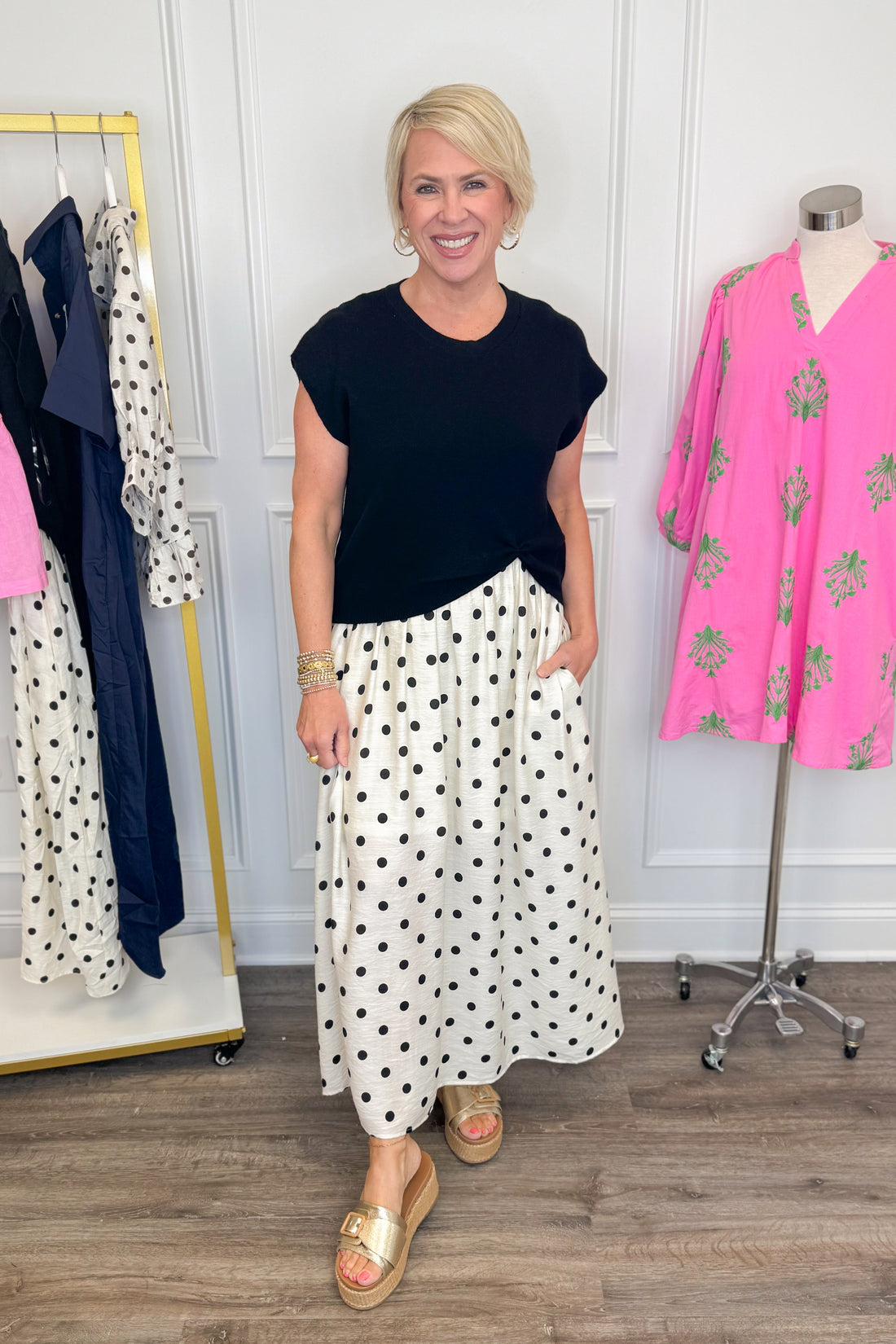Front view of woman wearing Swagger Boutique’s Black &amp; Cream Polka Dot Layered Midi Dress by Entro with sandals at the store. 